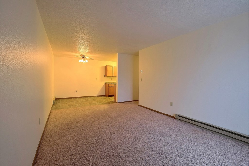 the living room and dining room of an empty apartment with white walls and carpet. Fargo, ND Village West Apartments