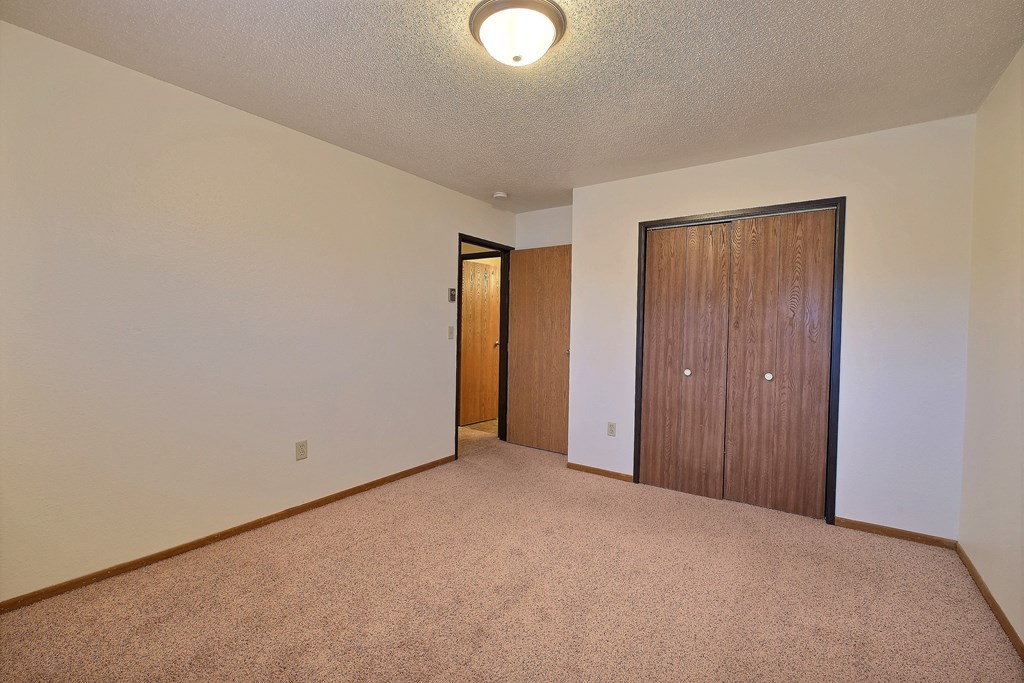 a spacious living room with carpet and a door to a bedroom. Fargo, ND Village West Apartments