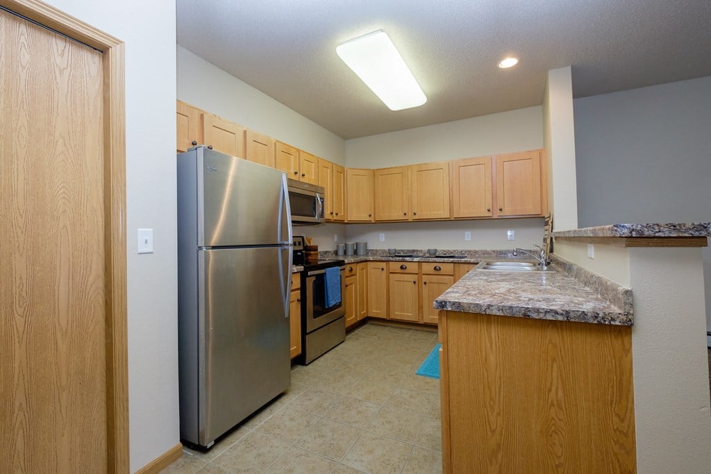 A large kitchen with stainless steel appliances and granite counter tops. West Fargo, ND West Lake Apartments