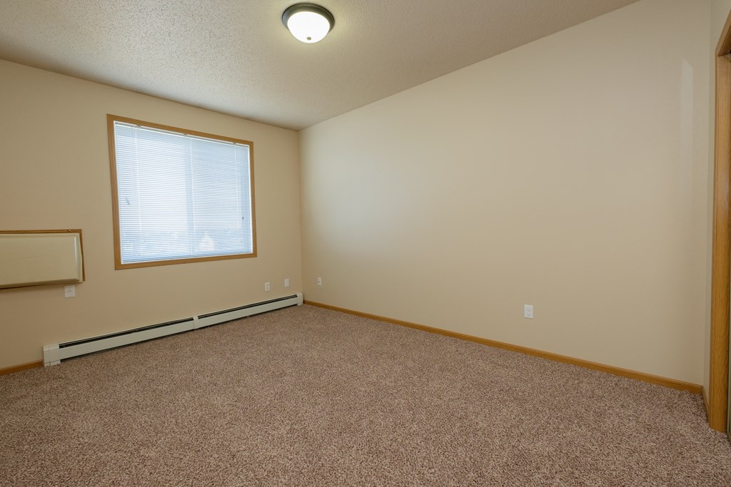 An empty bedroom with carpet and a window. West Fargo, ND West Lake Apartments.