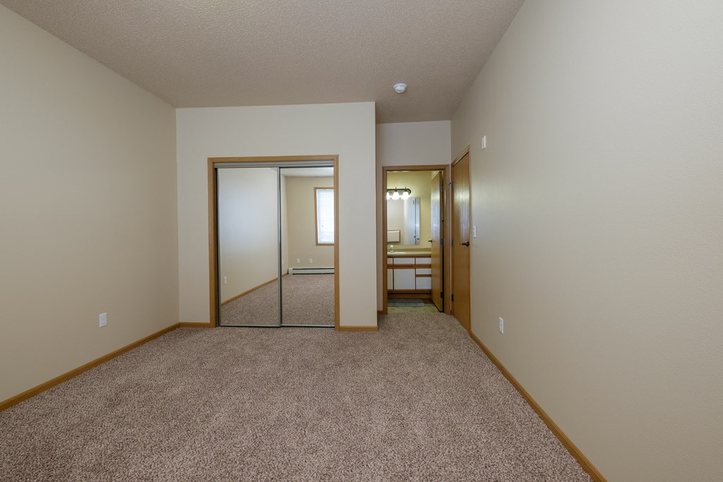 A bedroom with carpet and a mirror on the closet door. West Fargo, ND West Lake Apartments.