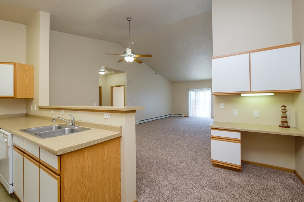 An empty kitchen and living room with a ceiling fan. West Fargo, ND West Lake Apartments.