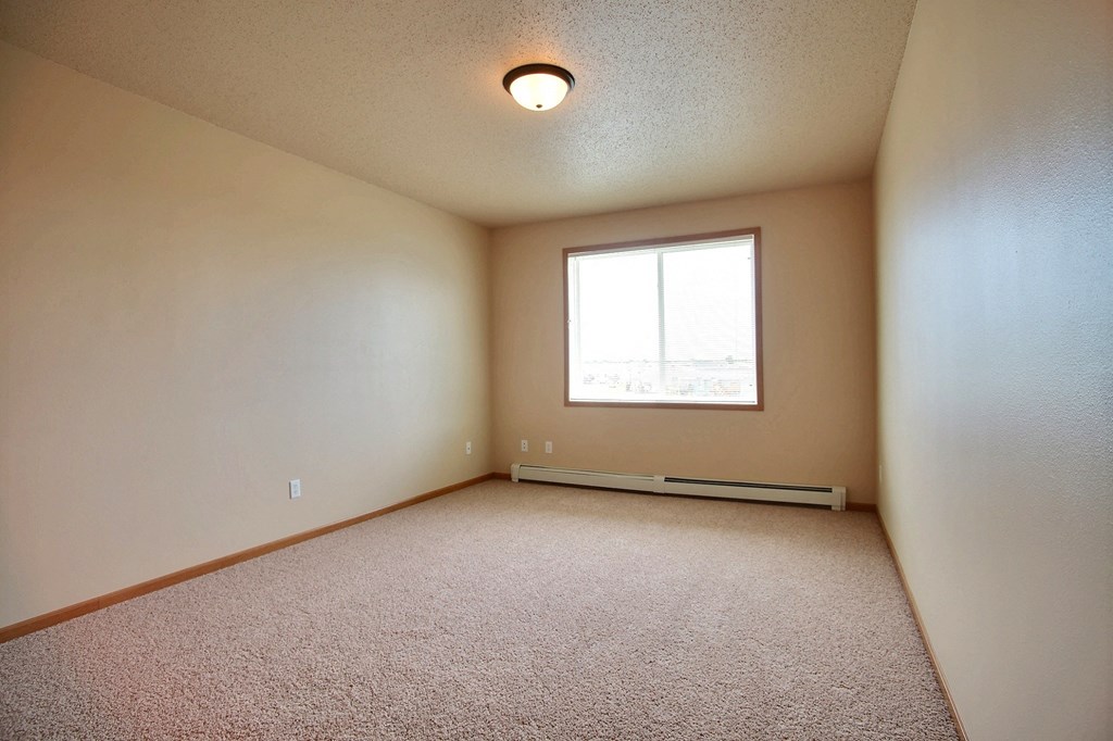 a bedroom with a window and a carpeted floor. West Fargo, ND West Lake Apartments.