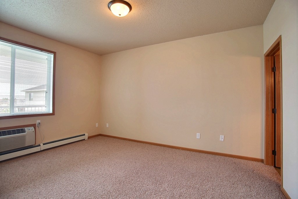 A bedroom with carpet and a window. West Fargo, ND West Lake Apartments.