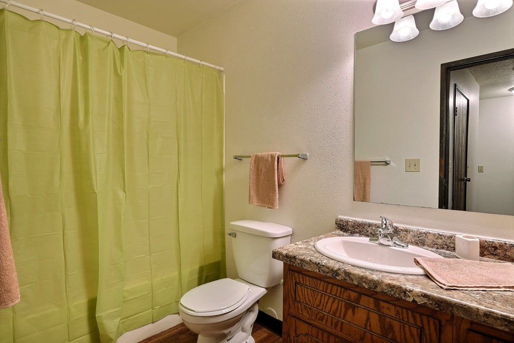 a bathroom with a green shower and a sink and a toilet. Fargo, ND Westcourt Apartments