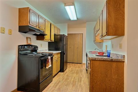 a kitchen with black appliances and wooden cabinets. Fargo, ND Westcourt Apartments