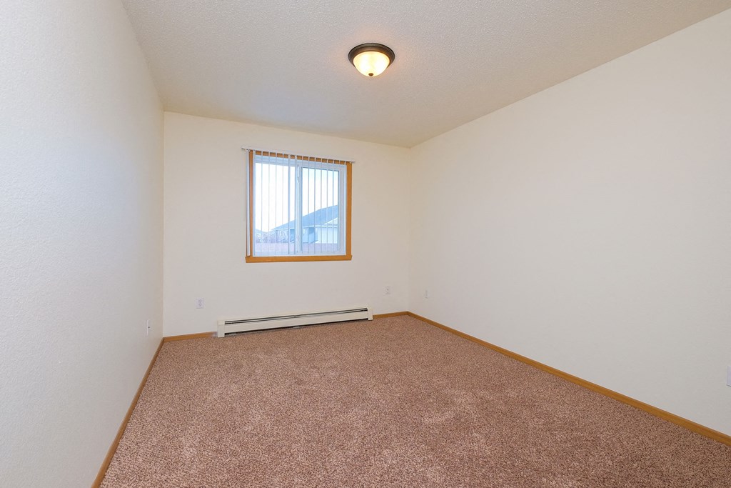 a bedroom with a window and a carpeted floor. Moorhead, MN Woodstone Apartments