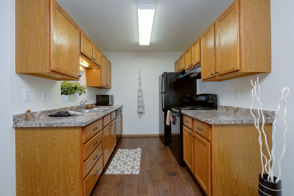 a kitchen with wood cabinets and black appliances and a counter top. Moorhead, MN Woodstone Apartments