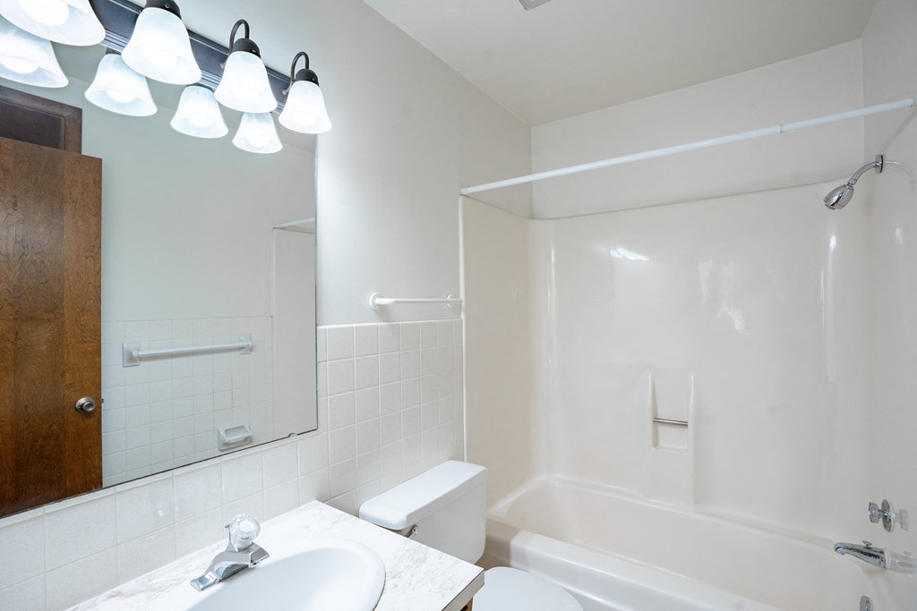 a white bathroom with a tub and a sink and a mirror. Fargo, ND Betty Ann Apartments