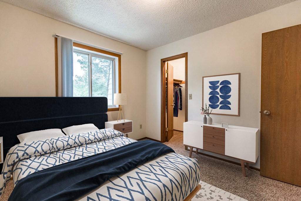 Bismarck, ND Brandon Apartments. A bedroom with a large bed with a blue and white comforter