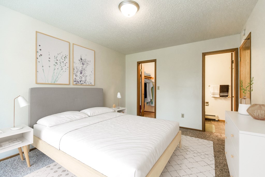 Bismarck, ND Brandon Apartments. The room showcases a comfortable bed with neatly arranged bedding and a calm ambiance. Soft lighting adds to the peaceful atmosphere, while a window allows natural light to fill the space. It's a tranquil retreat for rest and relaxation.