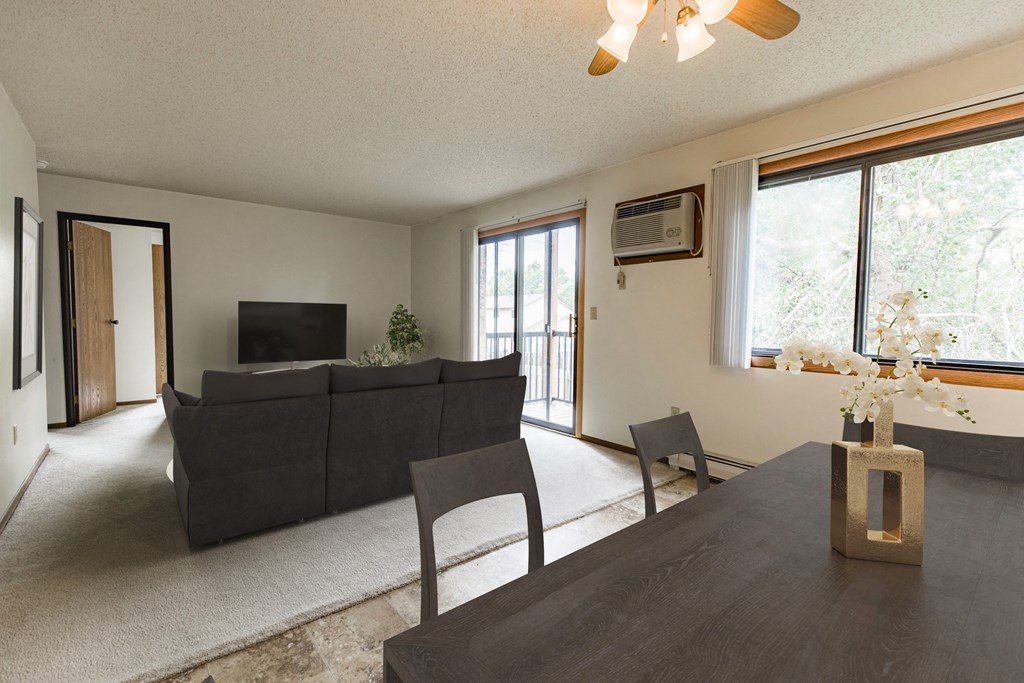 Bismarck, ND Eagle Sky I Apartments | Dining Bismarck, ND Eagle Sky I. A dining room with a black table with four chairs. The glass sliding door in the background brightens the room and living room behind the table with natural light.
