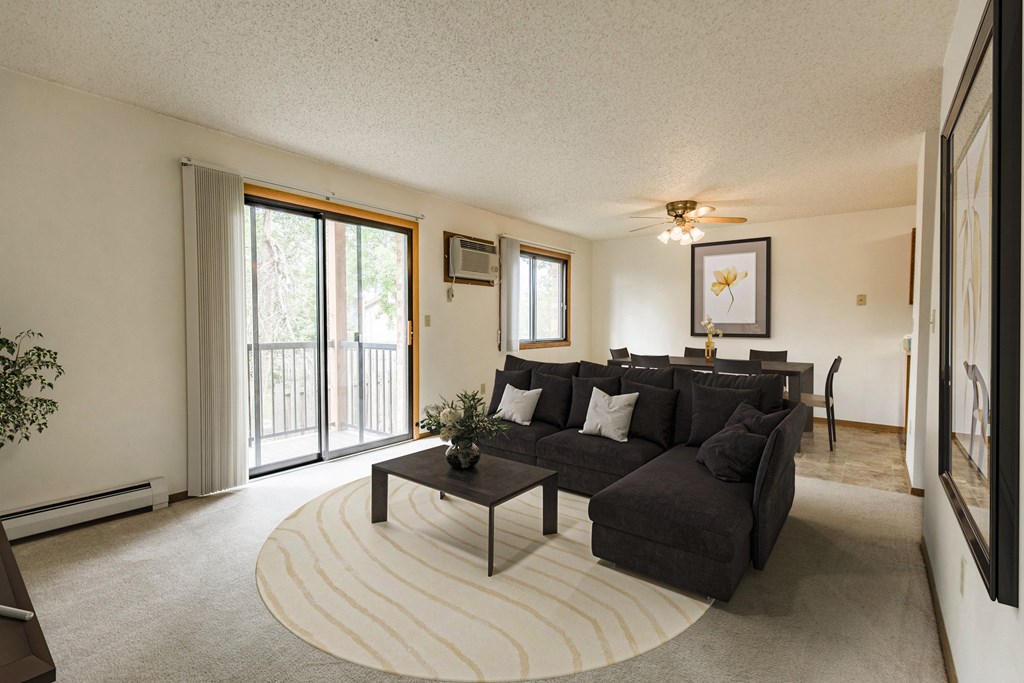 Bismarck, ND Eagle Sky I Apartments. a living room with a large couch and a coffee table in front of a sliding glass door that brightens the room