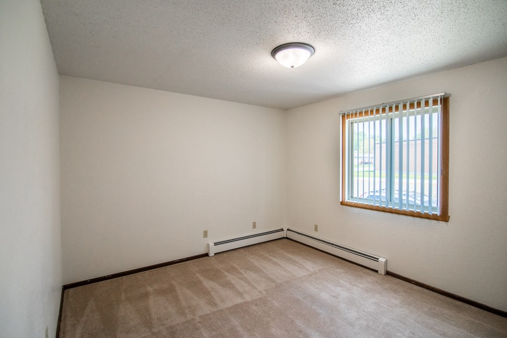 A bedroom with carpeted floors and a window. Bismarck, ND Eastbrook Apartments.