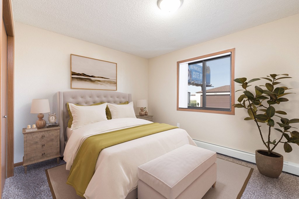 Bismarck, ND Fairview Apartments. A bedroom that showcases a comfortable bed with neatly arranged bedding, a stylish bed bench, and a window that fills the space with natural light. It's a serene and inviting setting for rest and relaxation.