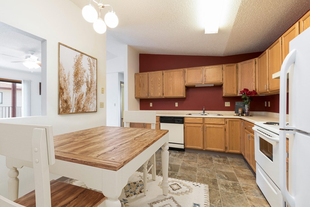 Bismarck, ND Fairview. A Kitchen that showcases appliances, a dining table with chairs, and a bold red accent wall. It's a stylish and inviting area for cooking and enjoying meals.
