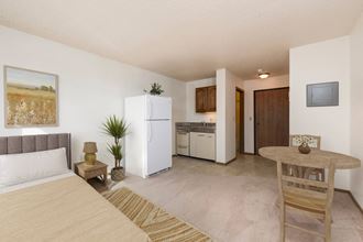 Mandan, ND Garden Grove Apartments. A bedroom area in a studio with a bed a table and a chair and a refrigerator