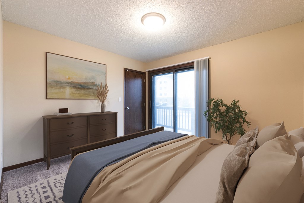Bismarck, ND Newgate Apartments.  a bedroom with a large bed and a dresser. A glass sliding door brightens with room with natural light.