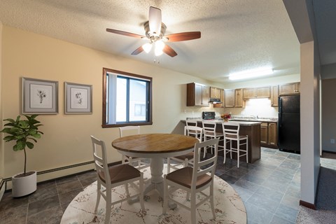 Bismarck, ND Newgate Apartment. a dining area with a table and chairs and a kitchen in the background. A small window illuminates the room