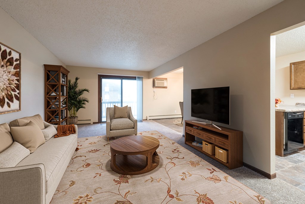 Bismarck, ND Newgate Apartments. A living room with a large rug, couch, and tv. A glass sliding door brightens the room with natural light