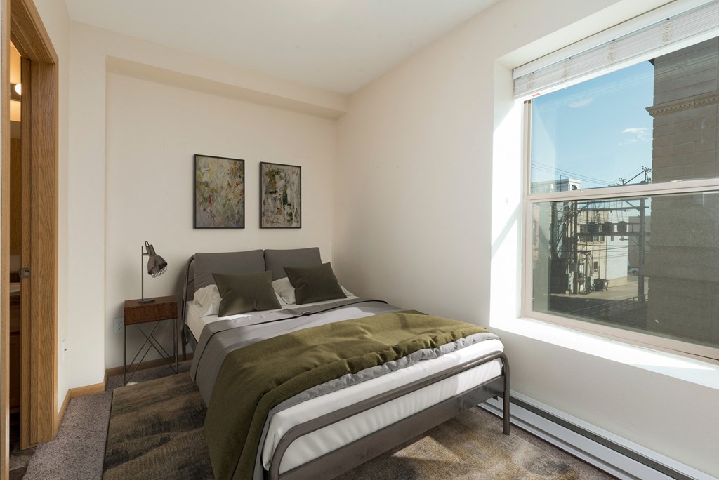 Bismarck, ND Norma Apartment serene bedroom featuring olive green bedding and a small window. The room exudes a tranquil ambiance