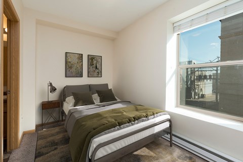 Bismarck, ND Norma Apartment serene bedroom featuring olive green bedding and a small window. The room exudes a tranquil ambiance