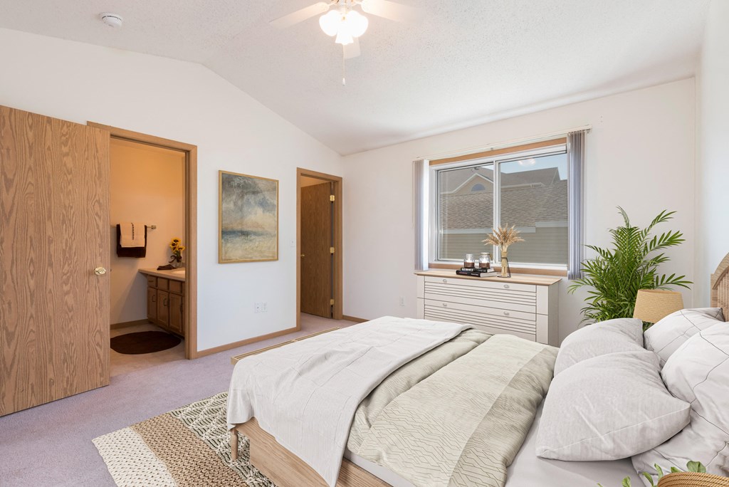 Bismarck Pebble Creek Apartments.  a bedroom with a large bed and a bathroom in the background. a large window fills the room with natural light