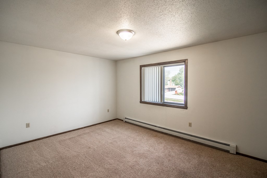 Bismarck, ND Rosser Apartments. a bedroom with a large window and beige carpet