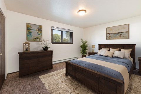 Bismarck, ND Rosser Apartments. A bedroom with dark wood bed, dresser, and night stands. A small window fills the room with natural light