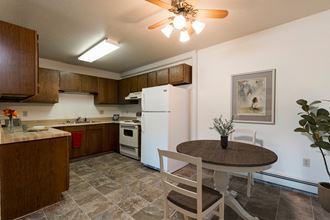 Bismarck, ND Rosser Apartments. A dining room with a table and two chairs. The overhead fan and light brighten the room. A kitchen with a white refrigerator freezer next to a white stove top oven are in the background