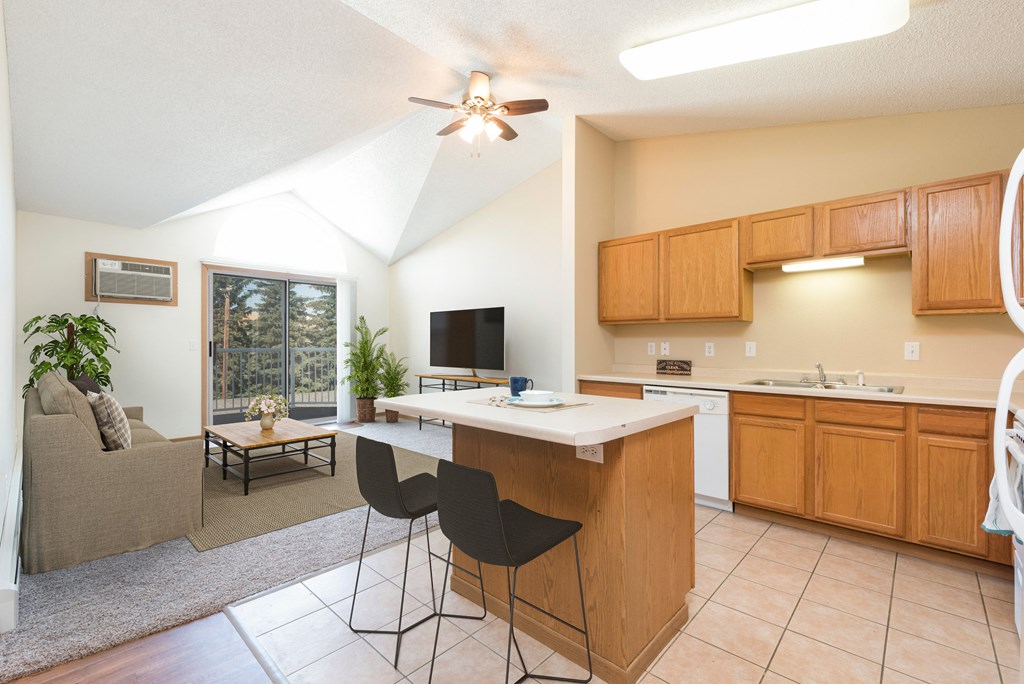 Bismarck, ND Sierra Ridge Apartments. The room is elegantly furnished with comfortable seating, bar stools, and tasteful decor, creating a welcoming and inviting atmosphere. The sliding glass door fills the room with bright natural light.