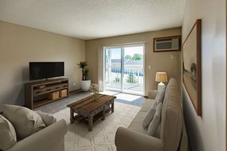 Bismarck, ND Sunset Ridge Apartments.  A living room with a couch, coffee table, tv, and a glass sliding door that brightens the room with natural light.