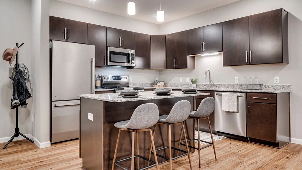 a kitchen with stainless steel appliances and a counter with three bar stools. Circle Pines, MN Lexington Lofts