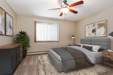a cozy bedroom in Parkview Estates, Coon Rapids. The room features a comfortable bed with neatly arranged bedding and a relaxing ambiance. Soft lighting and a ceiling fan add to the soothing atmosphere, creating a tranquil space for rest and sleep