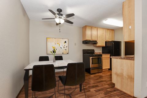 a cozy dining area in Parkview Estates, Coon Rapids. The room features a simple dining table and four chairs, set in a warm and inviting ambiance. The kitchen in the background has stainless steel appliances.