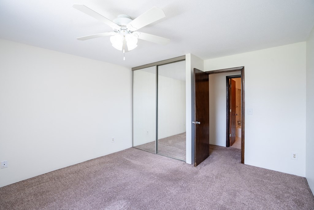 a bedroom with a ceiling fan and mirrored closet. Coon Rapids, MN Robinwood Apartments