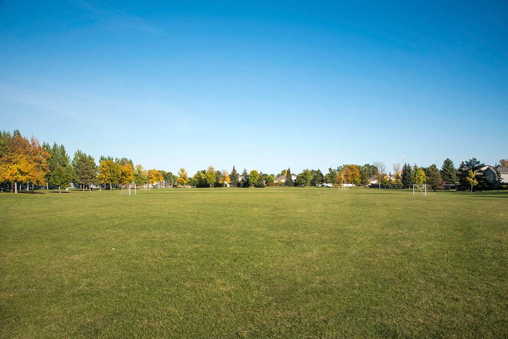 A large grassy field with trees in the background. Fargo, ND Stonebridge Apartments