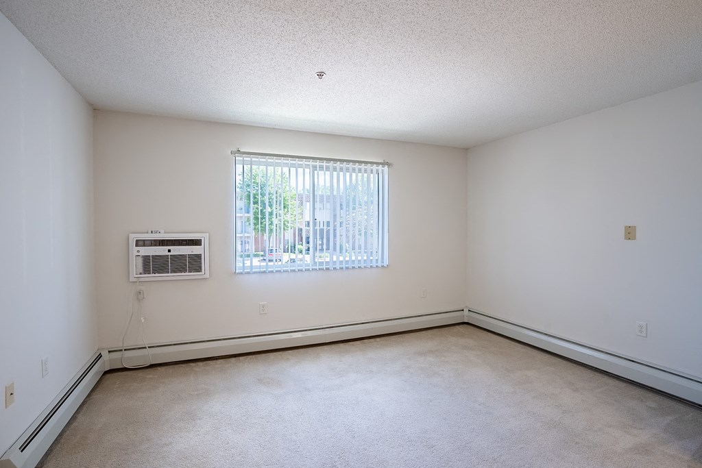 the living room of an empty house with a window and white walls. Eagan, MN Glen Pond Apartments