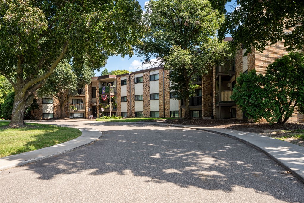 A tree-lined street with a building in the background. White Bear Lake, MN White Bear Terrace Apartments