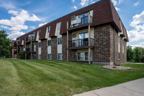 A brick apartment building with balconies and a green lawn in front. Bismarck, ND Belmont West Apartments