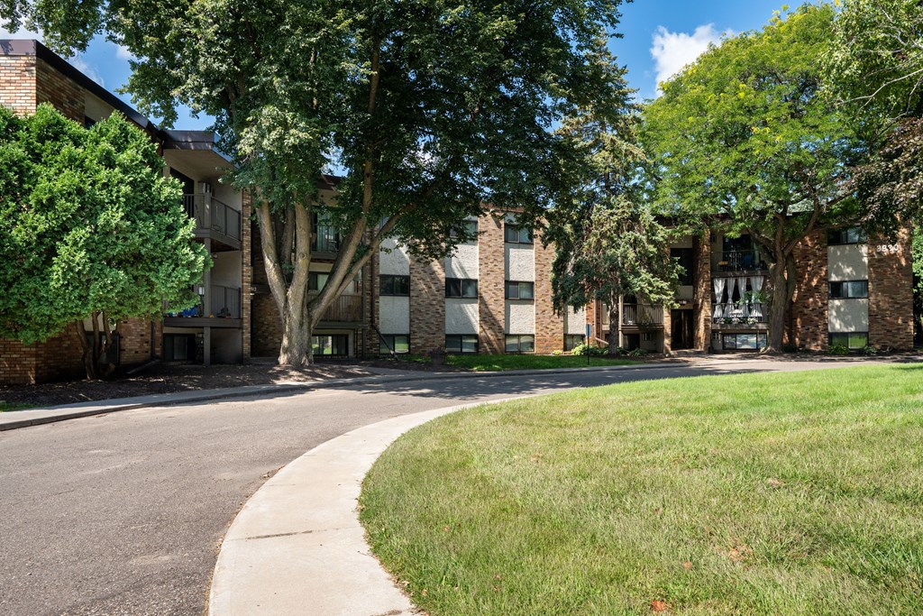 A tree-lined street in front of a brick building. White Bear Lake, MN White Bear Terrace Apartments