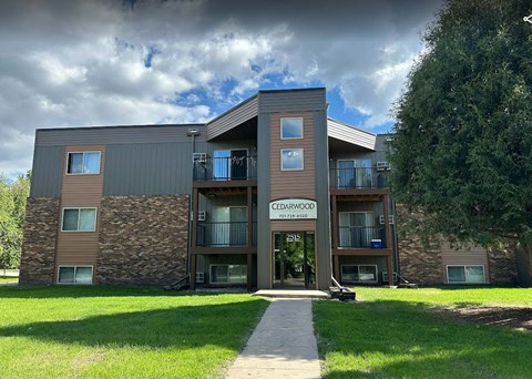 a modern building named Cedarwood with a signboard and a walkway leading to the entrance. Grand Forks, ND Cedarwood Apartments