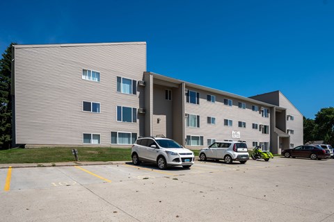 A grey building with a parking lot in front of it. Bismarck, ND Bradbury Apartments