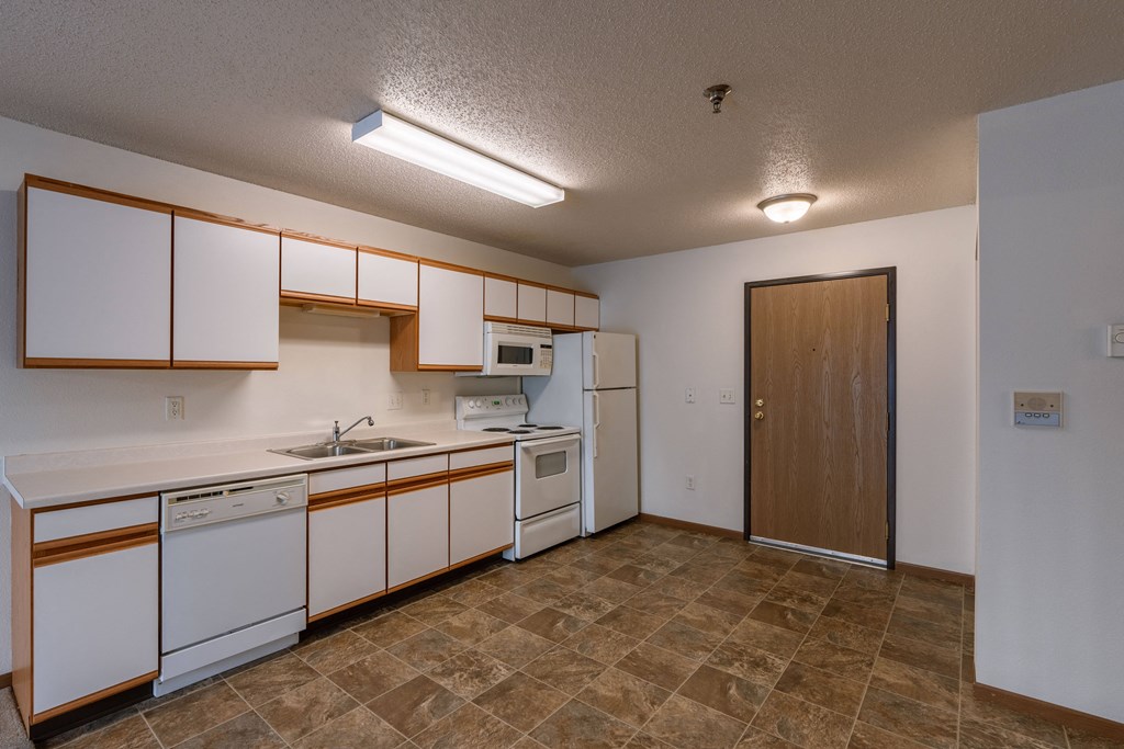 an empty kitchen with white appliances and wooden cabinets. Fargo, ND Lake Crest Apartments