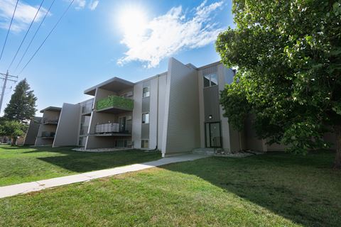 the exterior of an apartment building with grass and a sidewalk