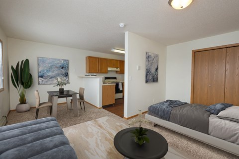 Fargo, ND Ashbury Apartments. a bedroom with a bed a table and a chair and a kitchen in the background