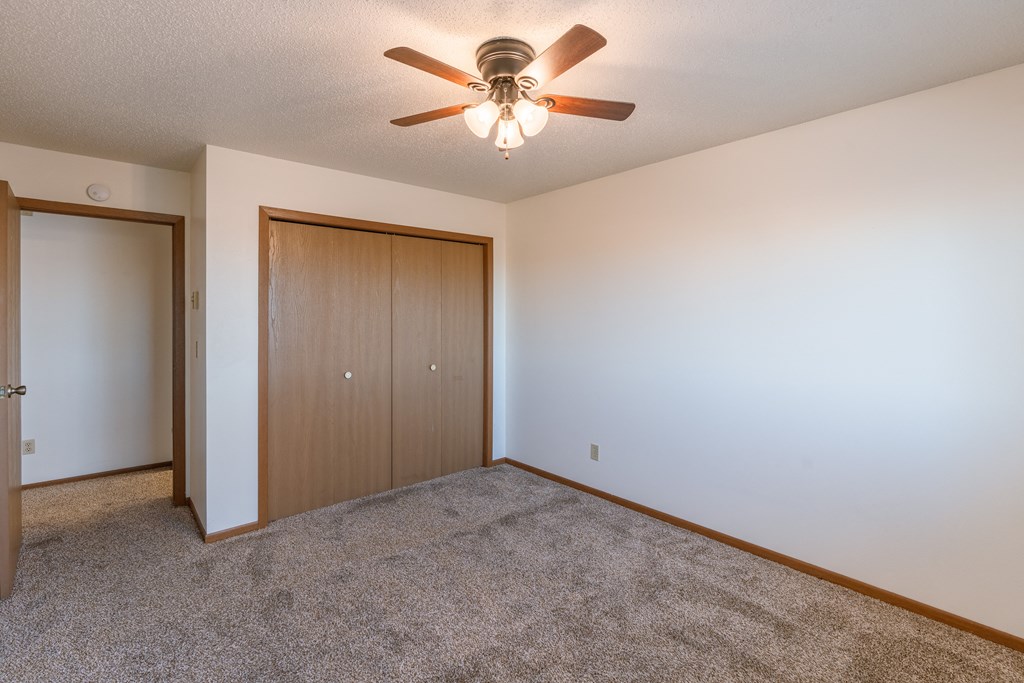 a bedroom with a ceiling fan and a closet. Fargo, ND Auburn II Apartments