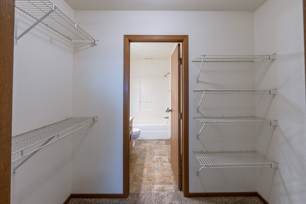an empty closet with empty shelves and an open door to a bathroom. Fargo, ND Auburn II Apartments