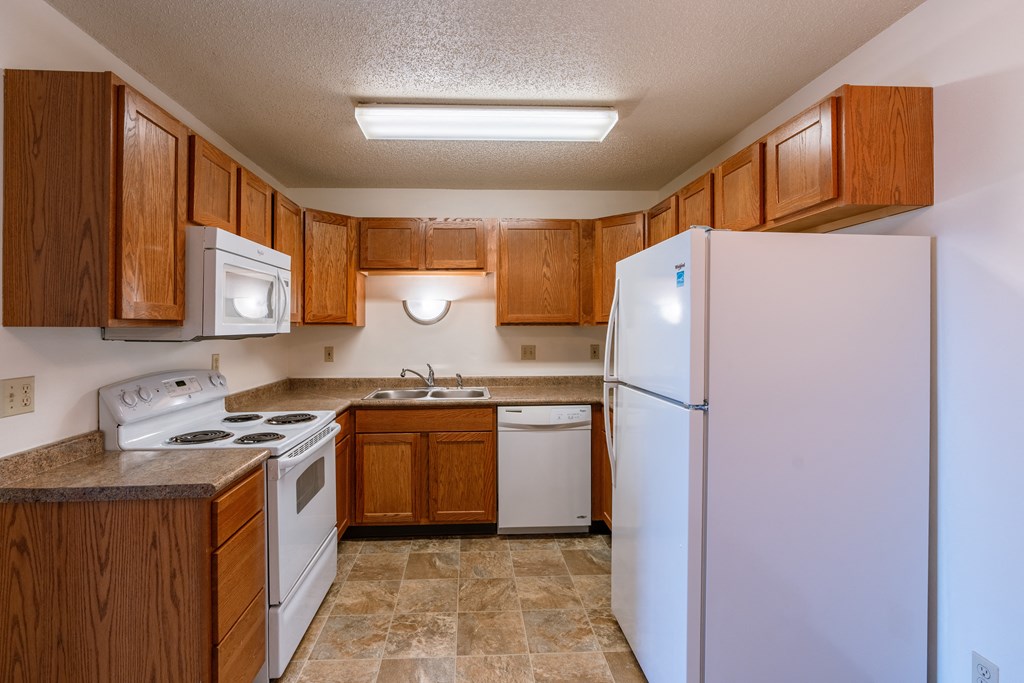 a kitchen with white appliances and wooden cabinets. Fargo, ND Auburn II Apartments