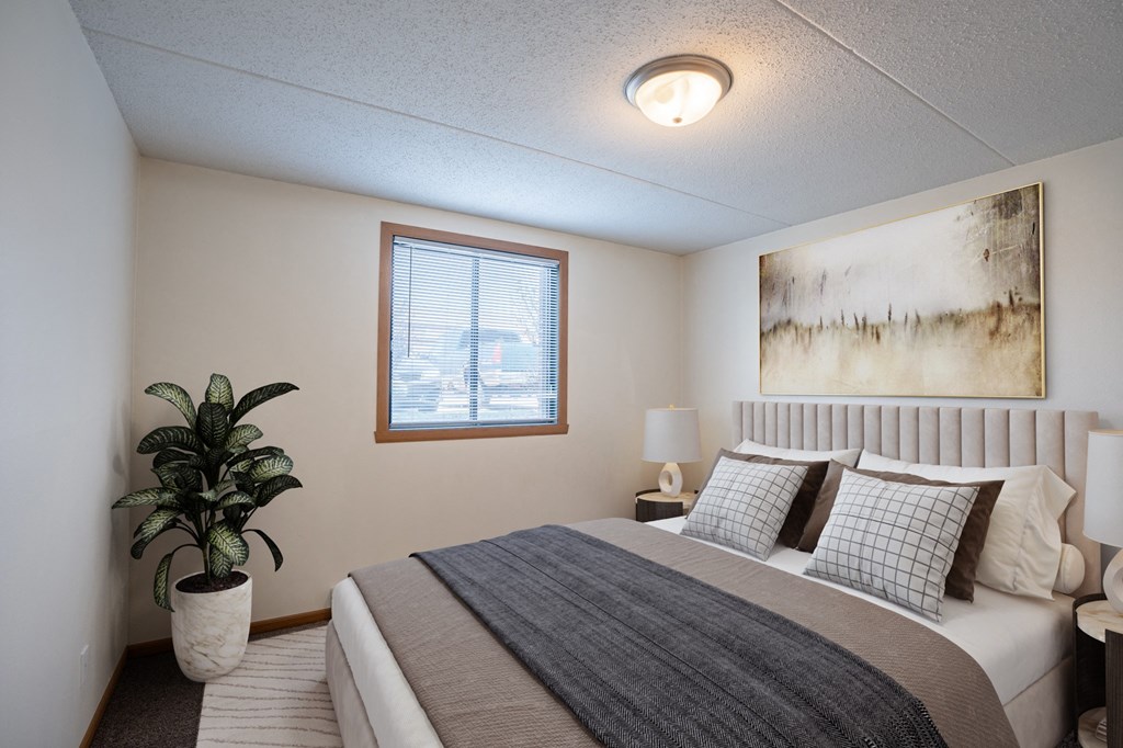 a bedroom with a bed and a potted plant and a window. Fargo, ND Bella Vista Apartments